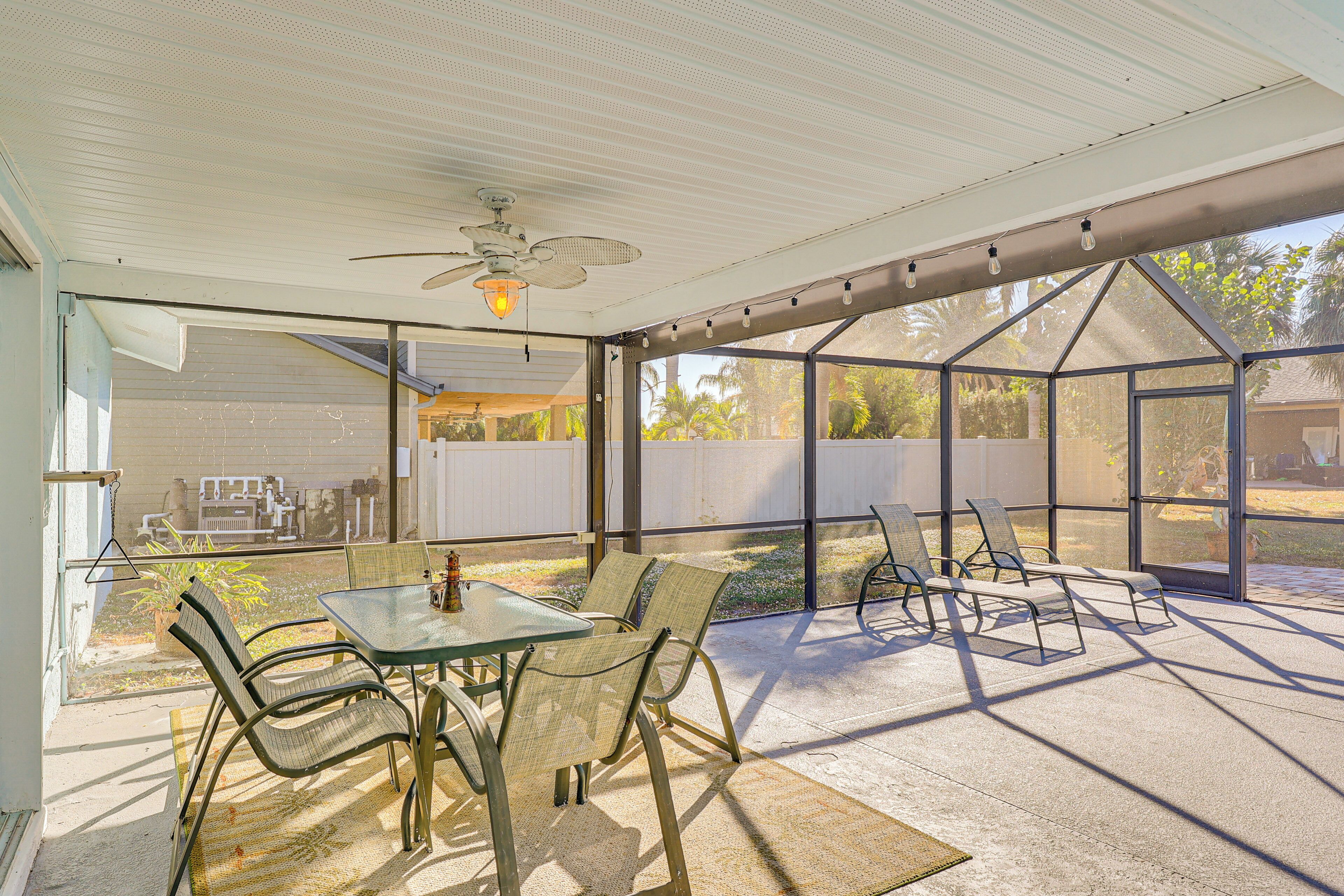 A covered patio with a glass table and chairs, a ceiling fan, and a view of a backyard.