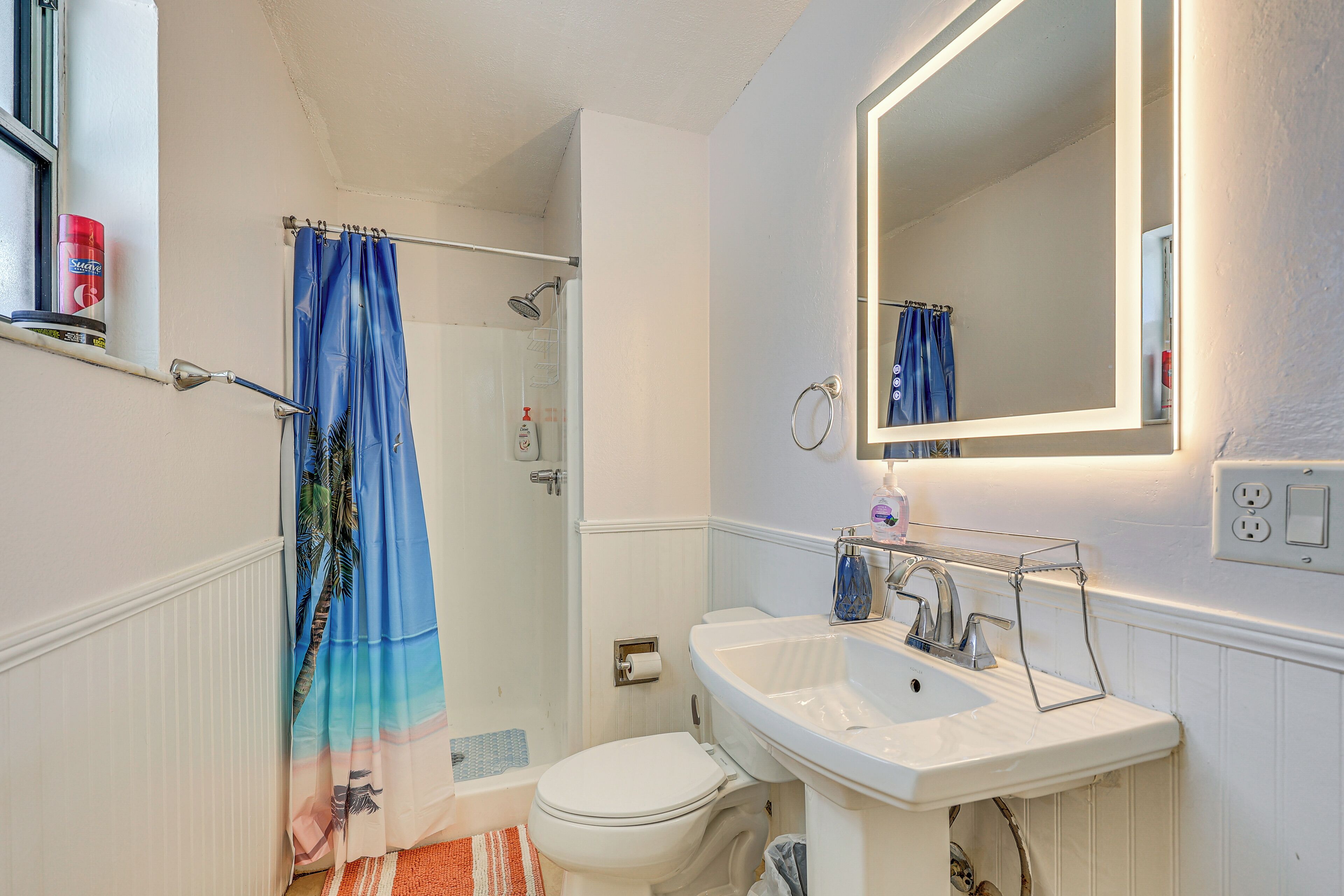 A bathroom with a white sink, a toilet, a shower with a blue curtain, and a mirror above the sink.