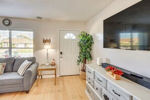 A living room with a gray sofa, a small wooden table, a white dresser, a large TV, and a potted plant. - Summer-ready North Port Home w/ Private Pool! (North Port)