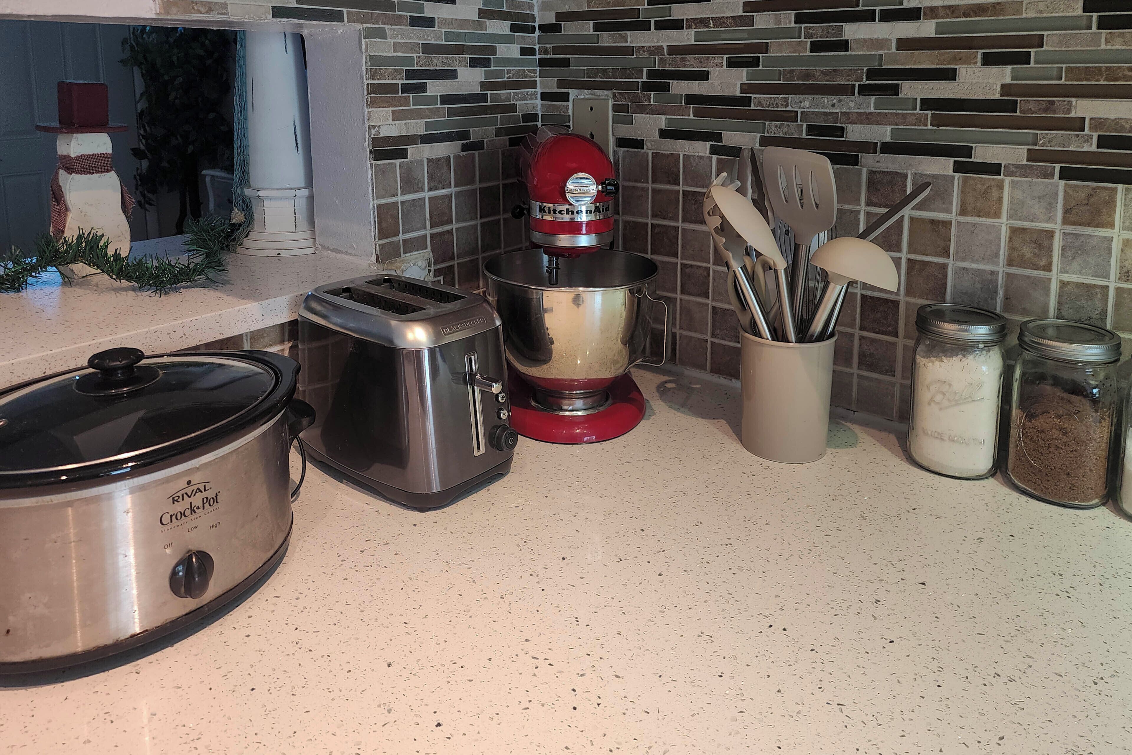 A kitchen with a slow cooker, toaster, mixer, and various utensils and containers.