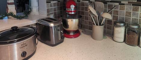 A kitchen with a slow cooker, toaster, mixer, and various utensils and containers.