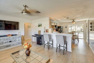 Amplia sala de estar con una mesa de centro de vidrio, una chimenea y un televisor. Cuenta con una zona de cocina con barra y asientos.