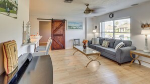 Un salon avec un piano, un canapé gris, une table basse et une grande fenêtre avec des stores.