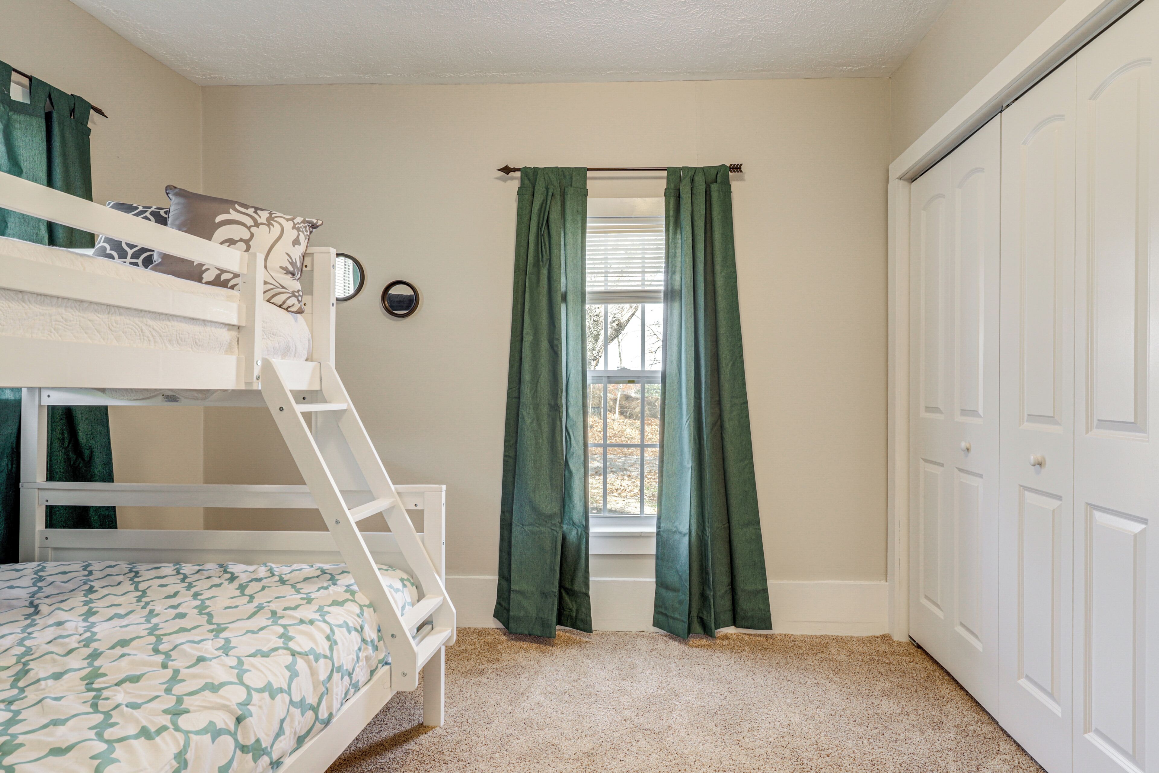 A room with bunk beds, a window with curtains, a door, and a carpeted floor.