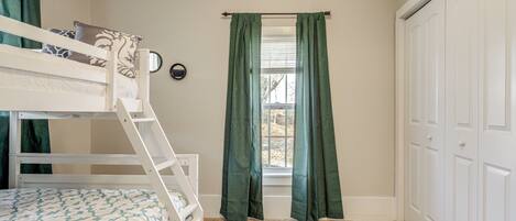 A room with bunk beds, a window with curtains, a door, and a carpeted floor.