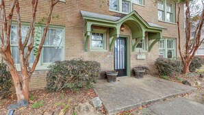 A two-story brick building with green trim around windows and doors, a front porch, and two large planters.