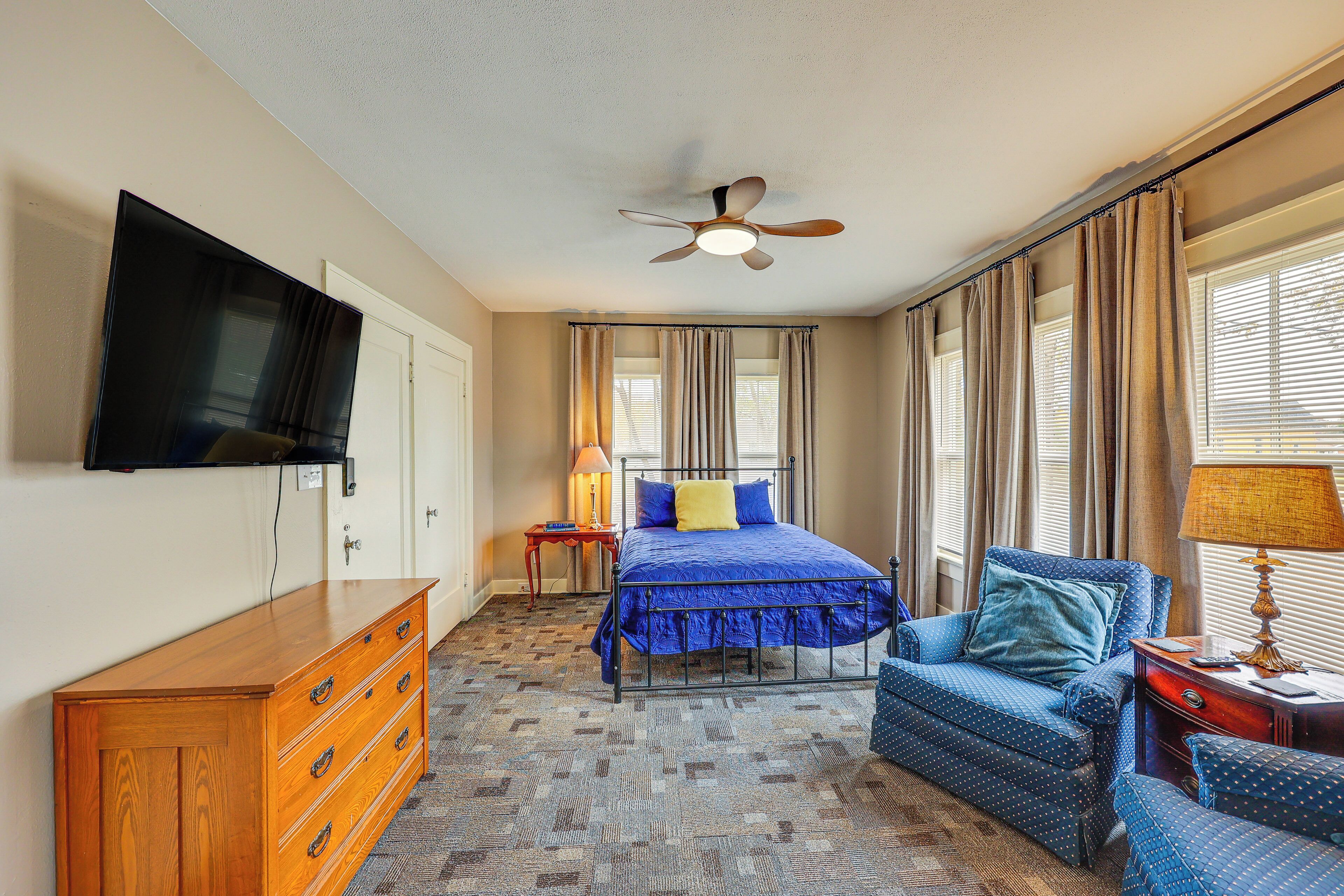 Una habitación de hotel con cama, televisión, cómoda de madera, silla y ventilador de techo.