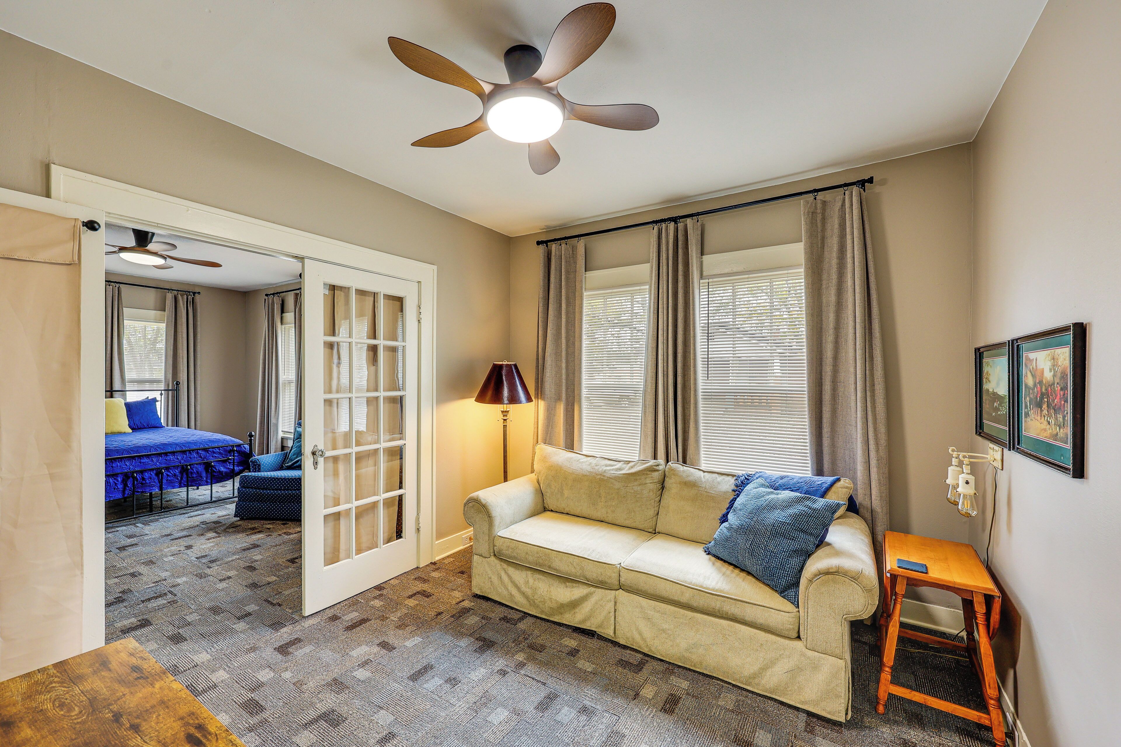 A room with a beige sofa, a wooden side table, a ceiling fan, and a door leading to another room.