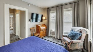 A bedroom with a bed, a chair, a dresser, a television, and a ceiling fan.