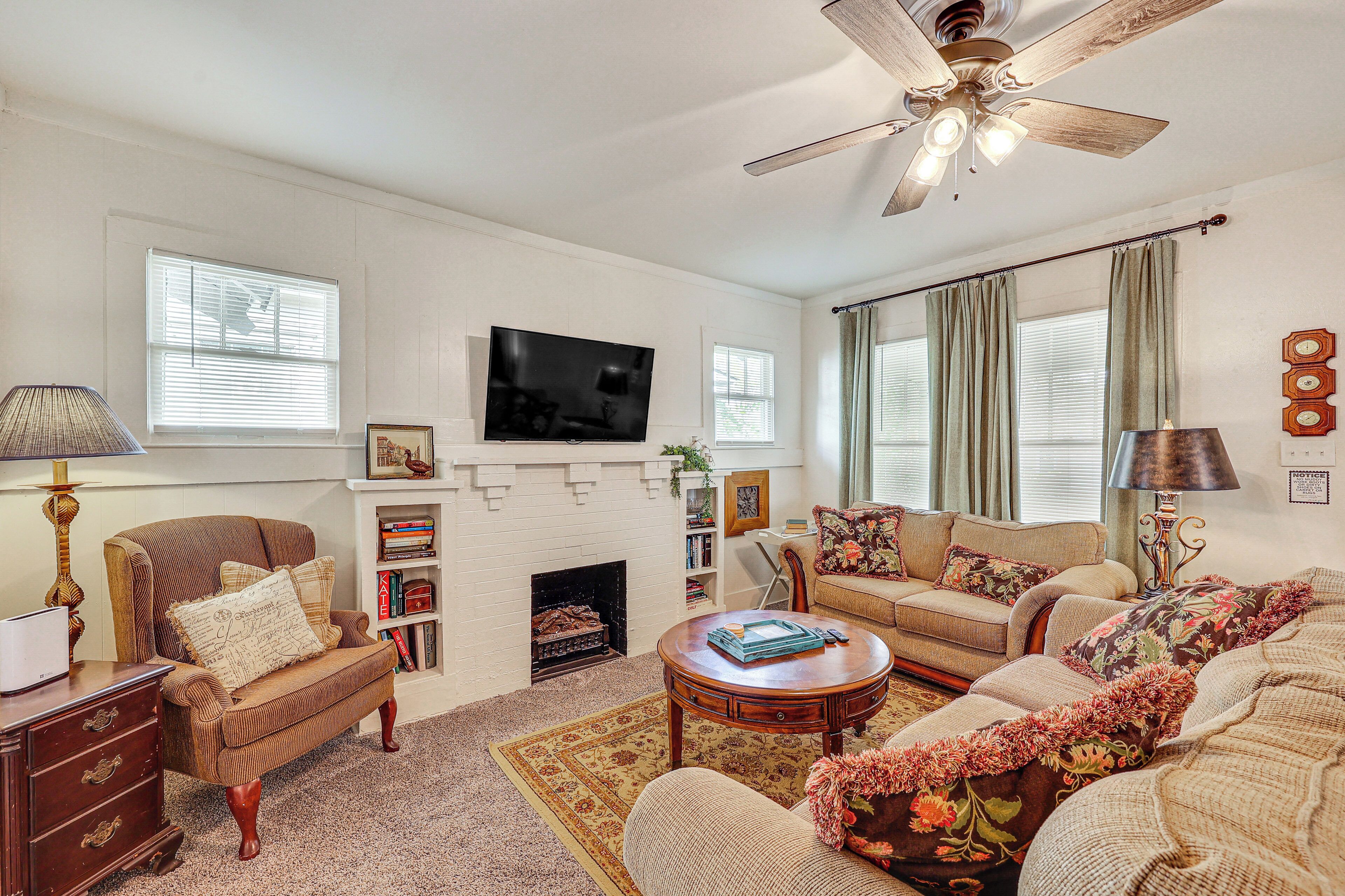 A living room with a fireplace, a television, and a ceiling fan.