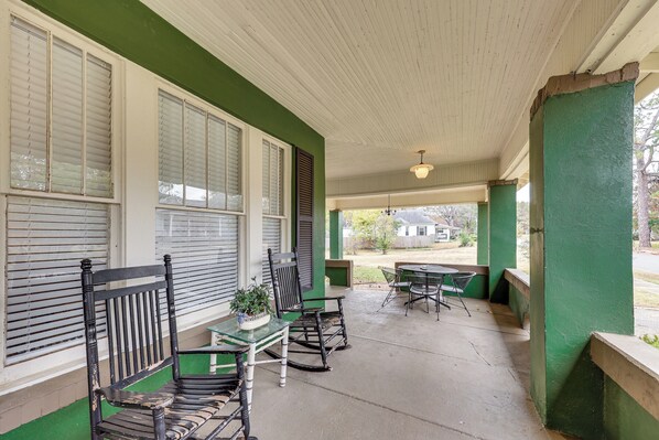 A covered porch with green walls, white trim, and a concrete floor. There are three rocking chairs and a small table with a potted plant. - Great for Gatherings! Gem < 1 Mi to Dtwn Texarkana (Texarkana)