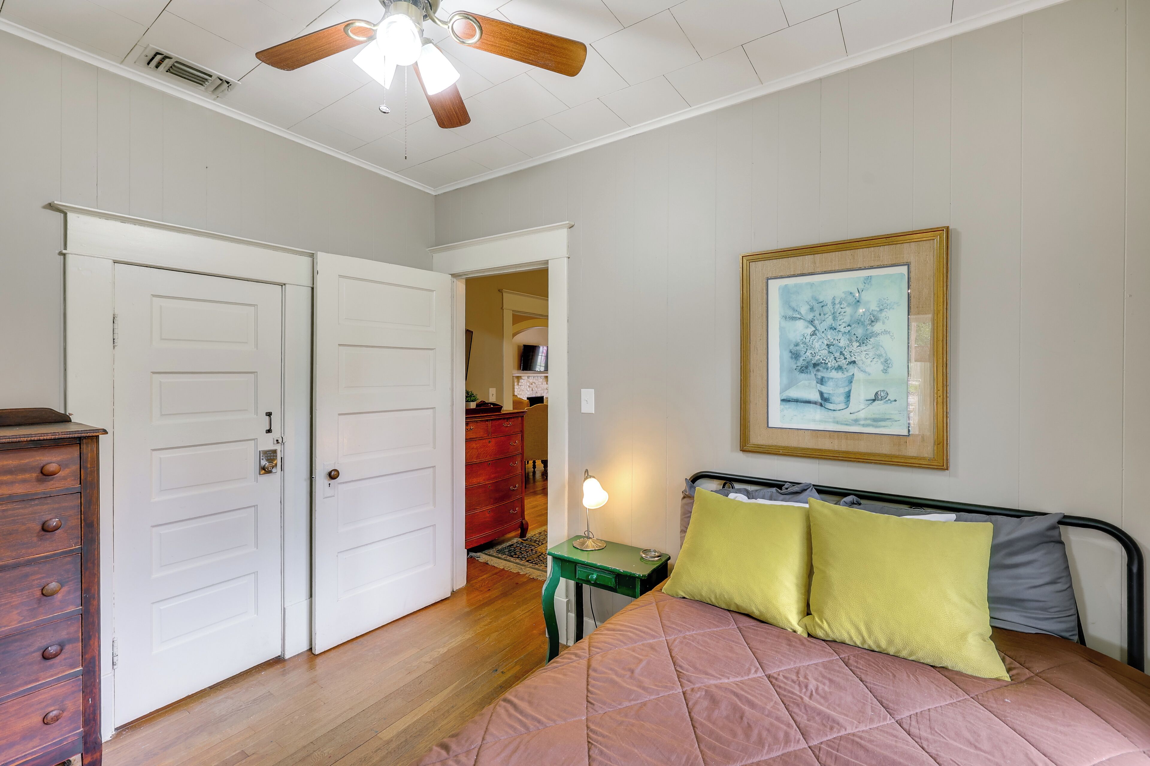 Une chambre à coucher avec un lit, un ventilateur de plafond, une commode et une porte.