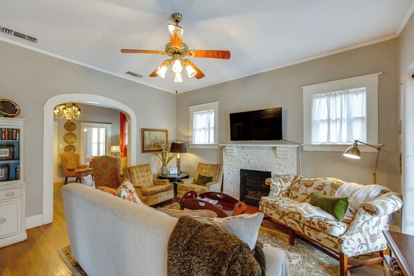 A living room with a fireplace, a ceiling fan, and a television mounted on the wall.