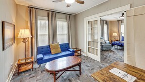 Une chambre d’hôtel avec un canapé bleu, une table basse en bois, un lampadaire et un ventilateur de plafond.