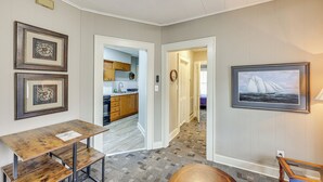 Une pièce avec une table et des bancs en bois, un tableau encadré au mur et une vue sur un coin cuisine.