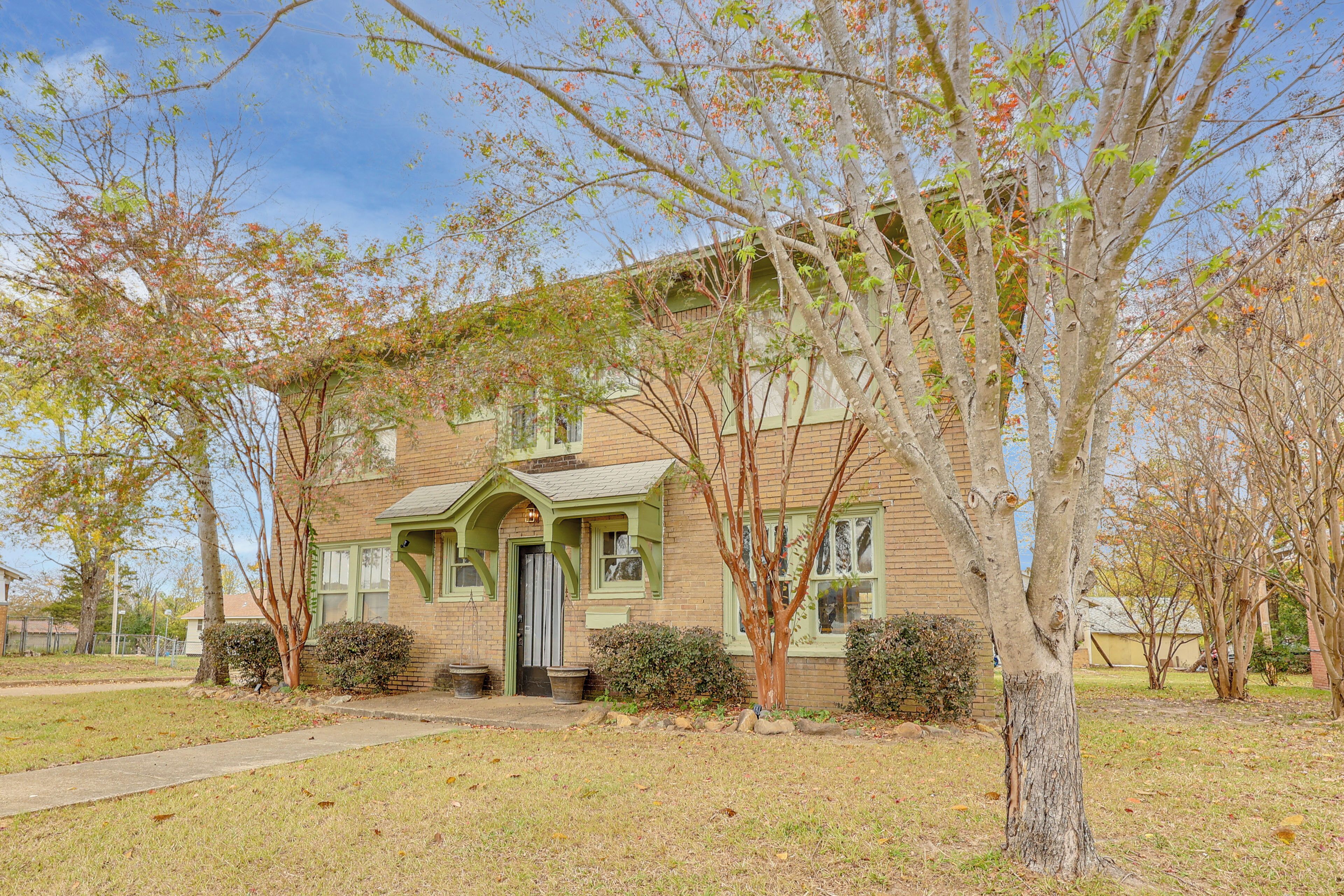 A two-story house with a front porch, a brick facade, and a small front yard with a tree and shrubs.