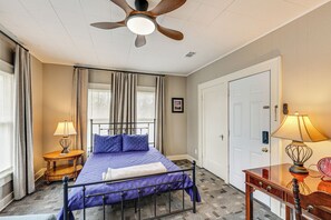 Quarto com cama, ventoinha no teto, mesa de cabeceira com luminária, escrivaninha com luminária e uma porta.