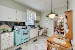 Une cuisine avec des meubles blancs, un poêle bleu et une table à manger en bois sur laquelle se trouve un panier.