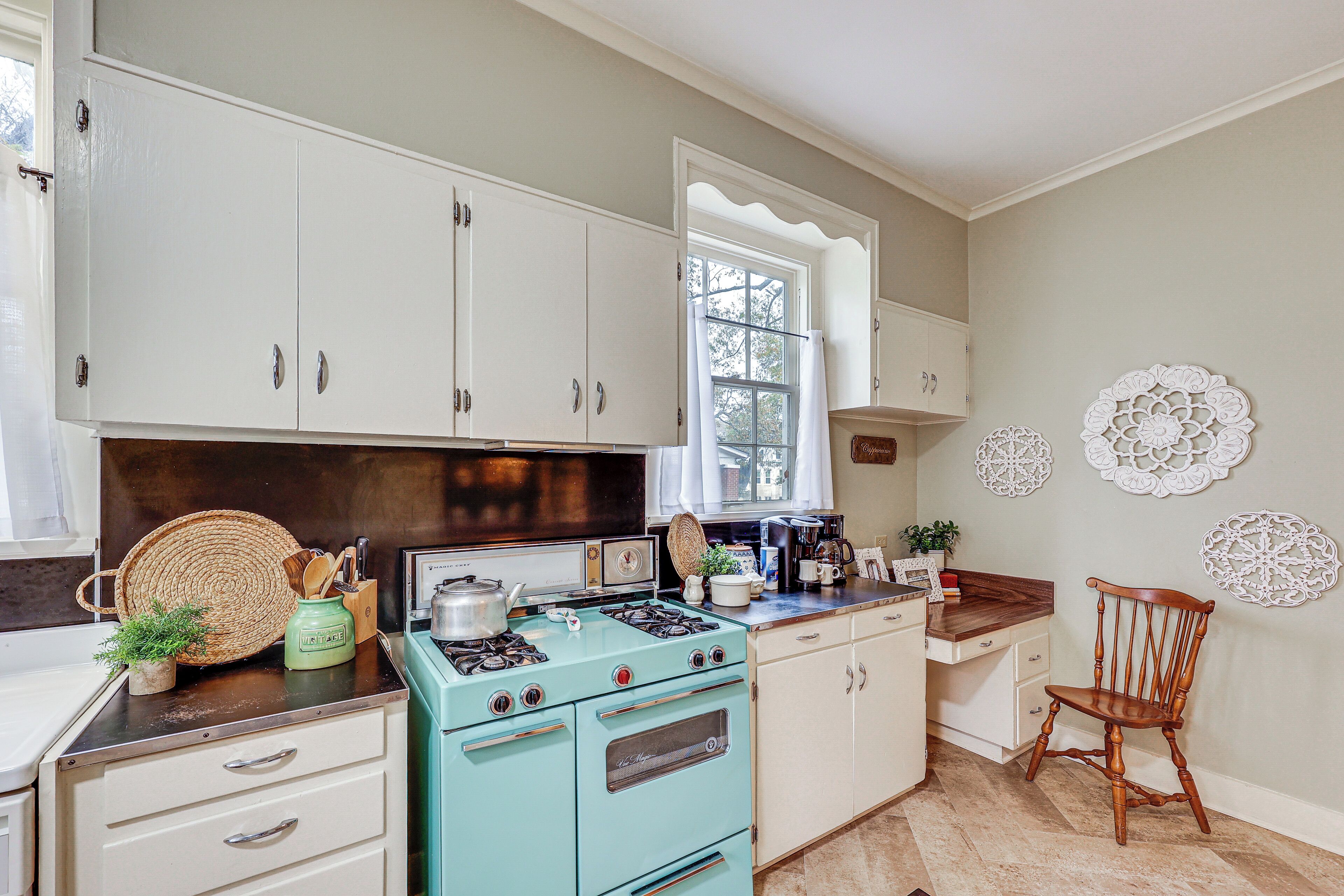 A kitchen with white cabinets, a teal stove, and a wooden chair.