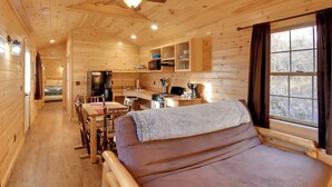 A cozy cabin interior with a dining area, kitchenette, and a large bed. - Shared Dock Access at Lakeside Sodus Bay Cabin! (North Rose)