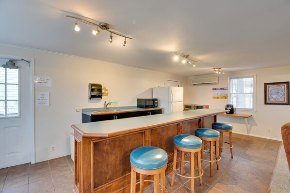 A kitchen with a bar area, wooden stools, a microwave, and a refrigerator. - Lakefront Cabin Living w/ Dock Access on Sodus Bay (North Rose)
