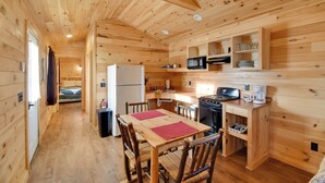 A wooden cabin interior with a kitchen, dining area, and a visible sleeping area. - Lakefront Cabin Living w/ Dock Access on Sodus Bay (North Rose)