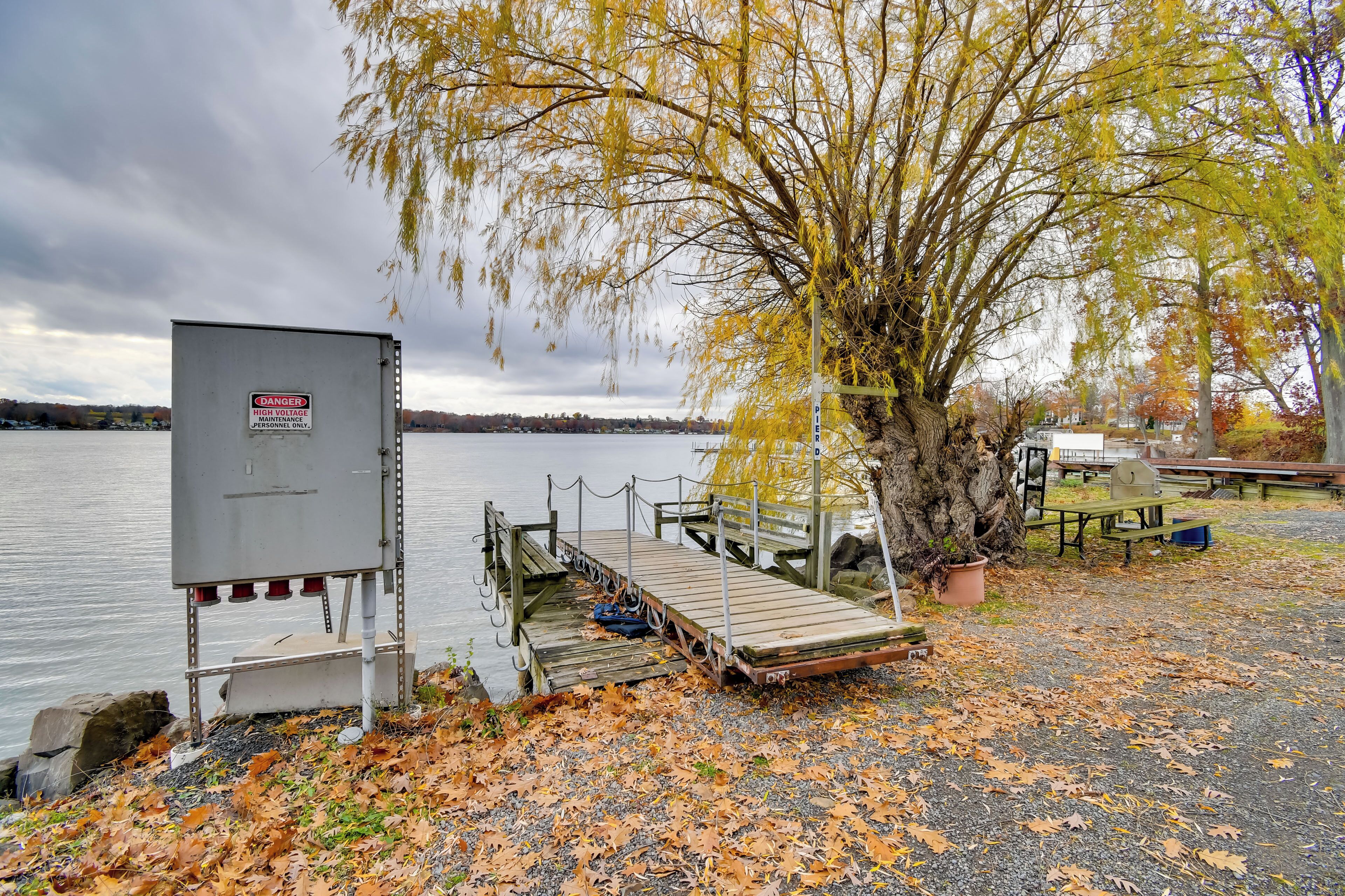 A dock extending into a lake with a warning sign, a picnic table, and a tree with yellow leaves.
