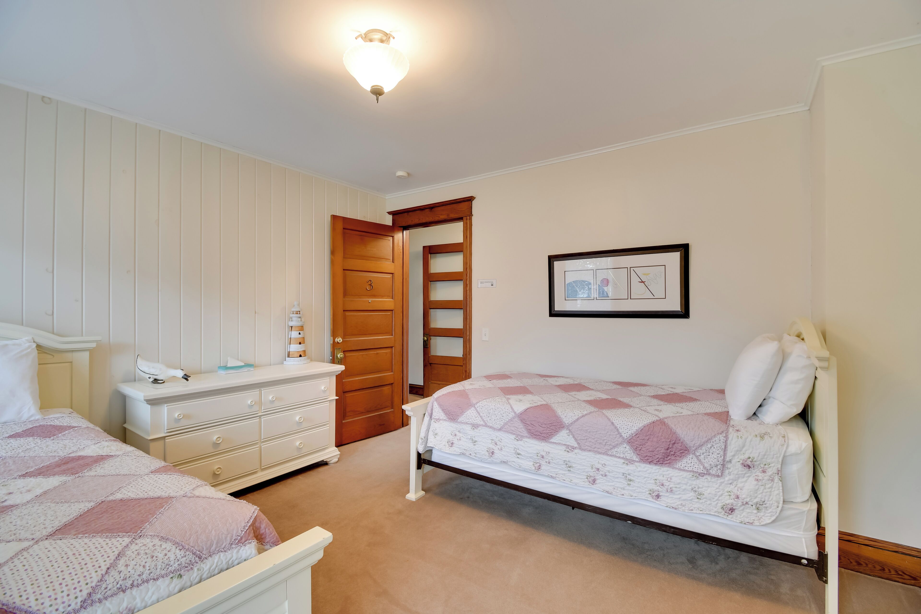 A bedroom with two beds, a dresser, and a door leading to another room.
