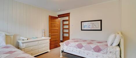 A bedroom with two beds, a dresser, and a door leading to another room.
