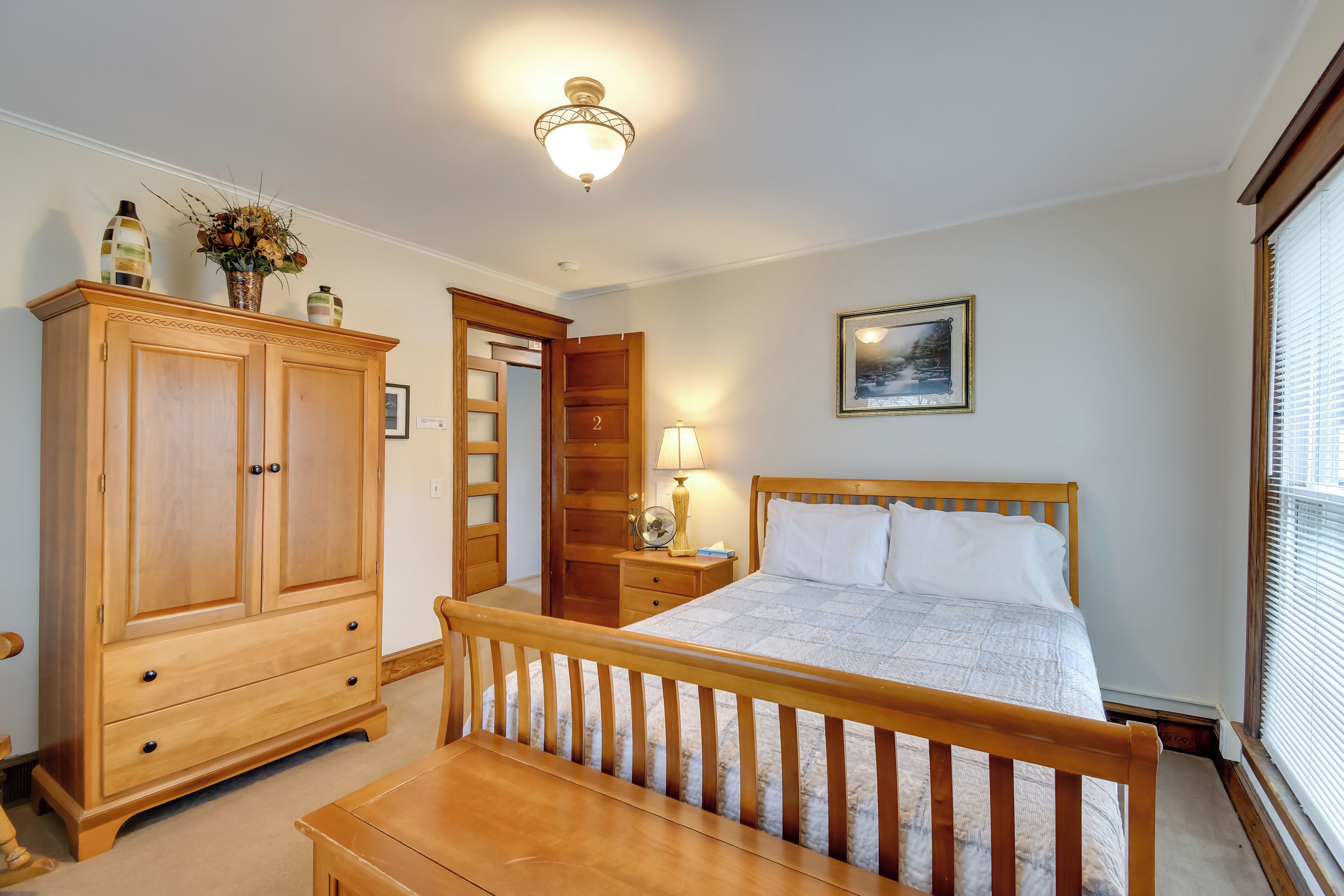 A bedroom with a wooden bed, a nightstand, a wardrobe, and a door leading to another room.