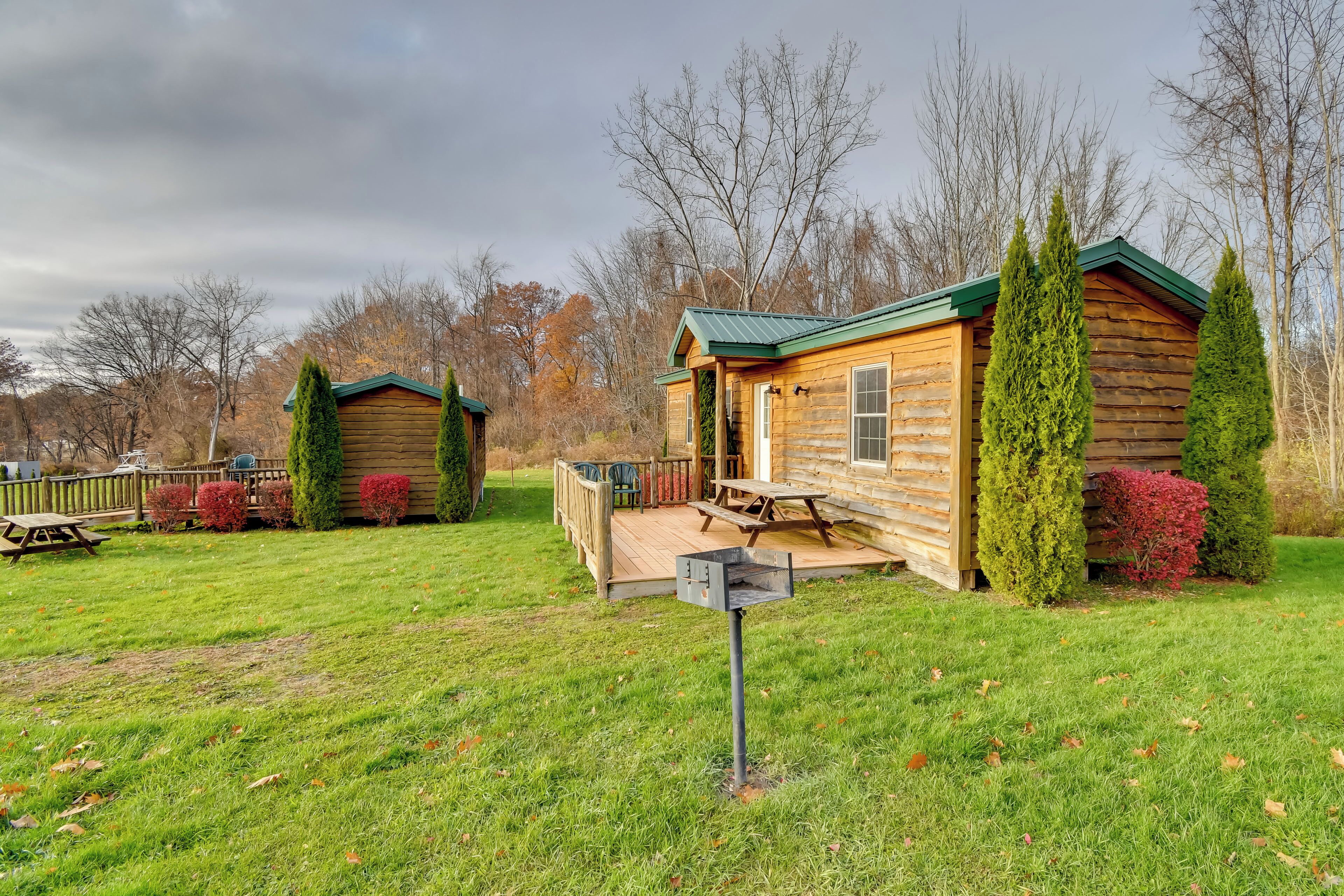 A log cabin with a deck, surrounded by a grassy yard and trees.