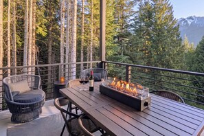 Une terrasse en bois avec un foyer, des sièges et une bouteille de vin.