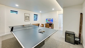 Een tafeltennistafel in een kamer met een televisie, lijstwerk en een klein kastje.
