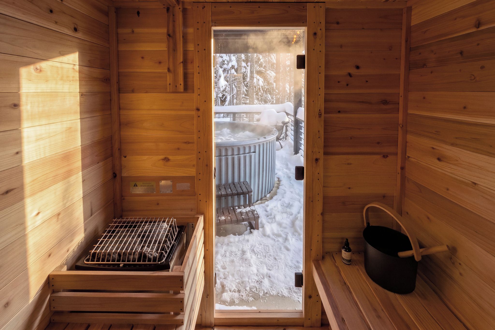 A wooden sauna room with a bench, a hot tub, and a bucket.