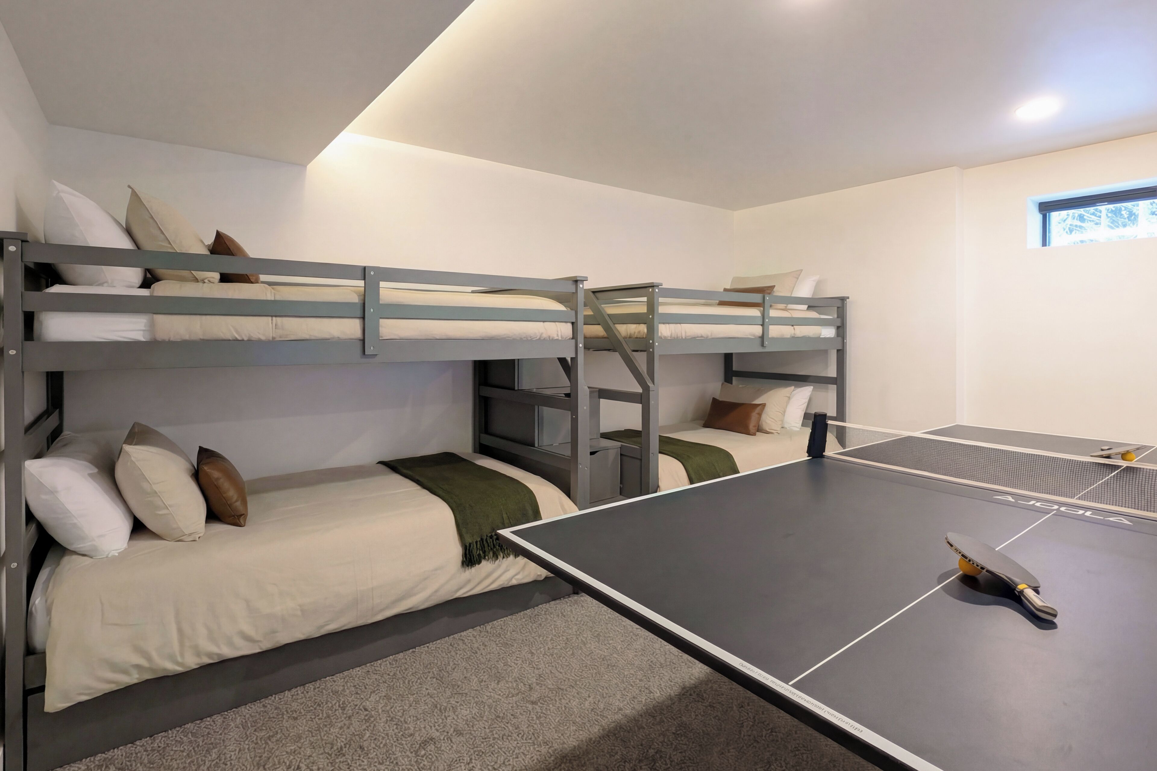 Una habitación con literas, una mesa de ping pong y una ventana pequeña.