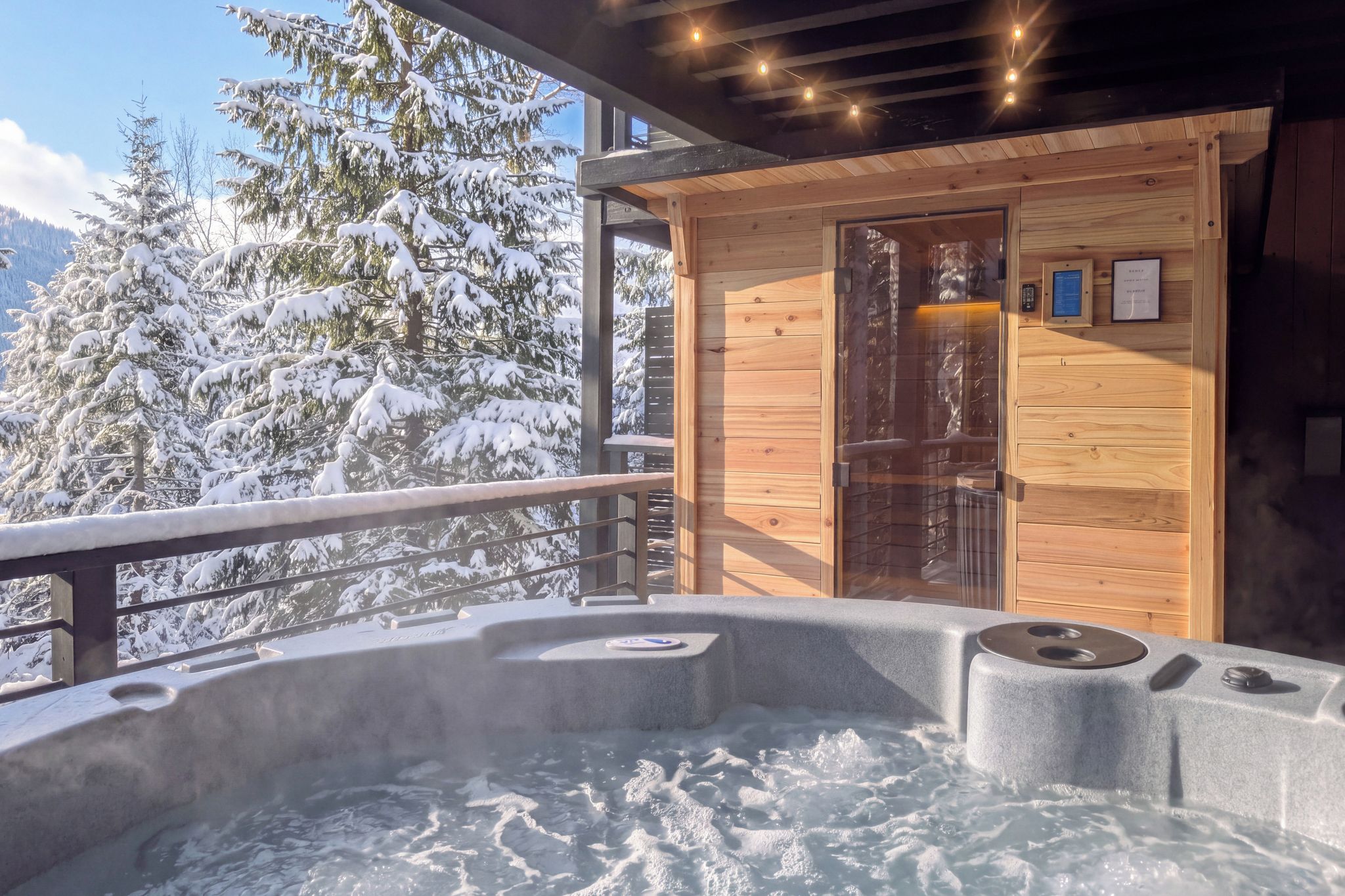 A hot tub with a wooden cabin in the background, surrounded by snow-covered trees.