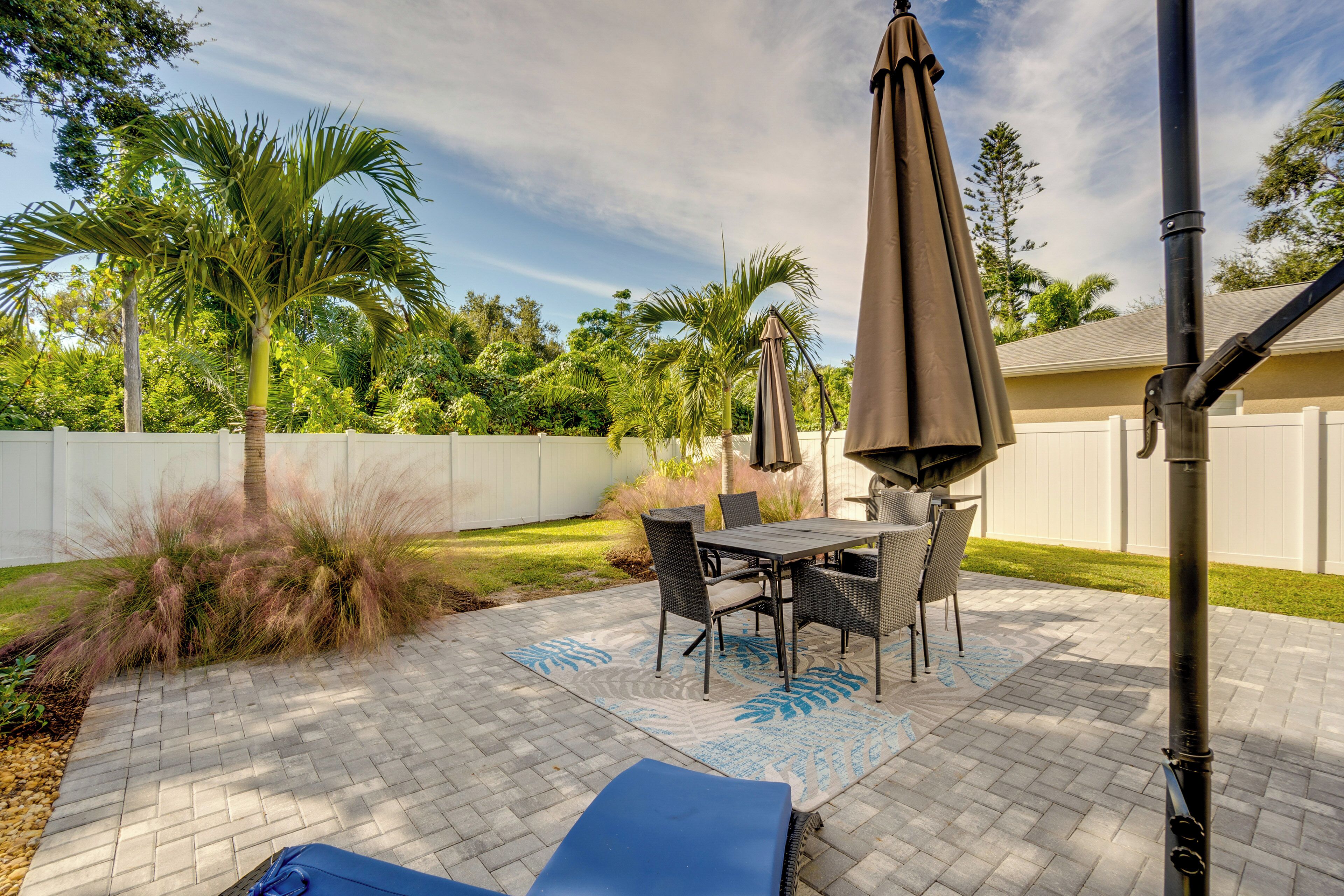 An outdoor patio with a table and chairs, surrounded by a white fence and lush greenery.