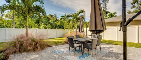 An outdoor patio with a table and chairs, surrounded by a white fence and lush greenery.