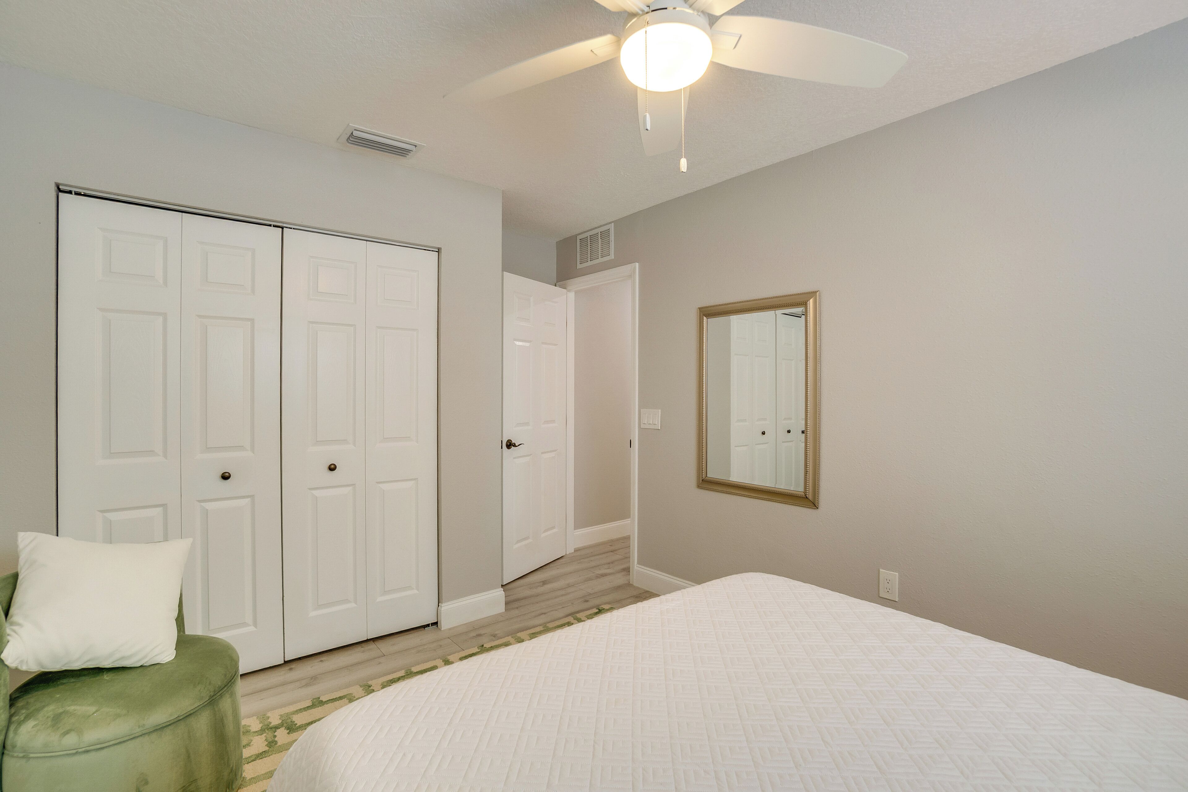 Un dormitorio con cama, una silla verde, ventilador de techo y un armario blanco.