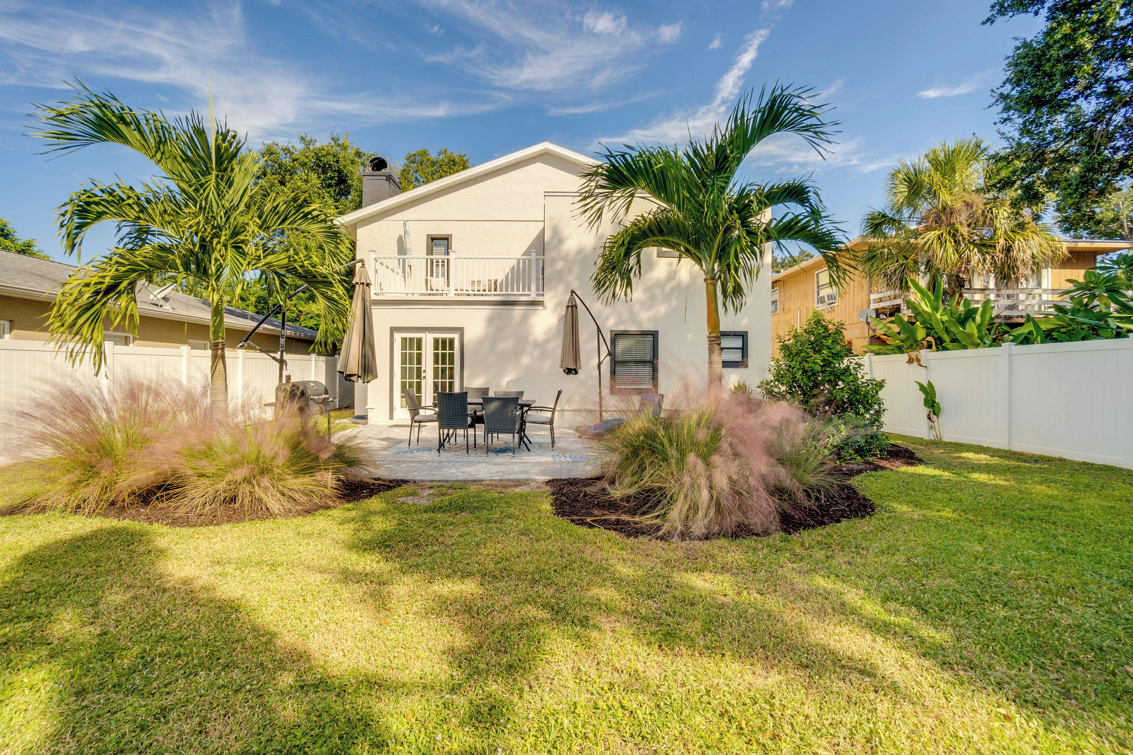A two-story house with a patio, palm trees, and a white fence.