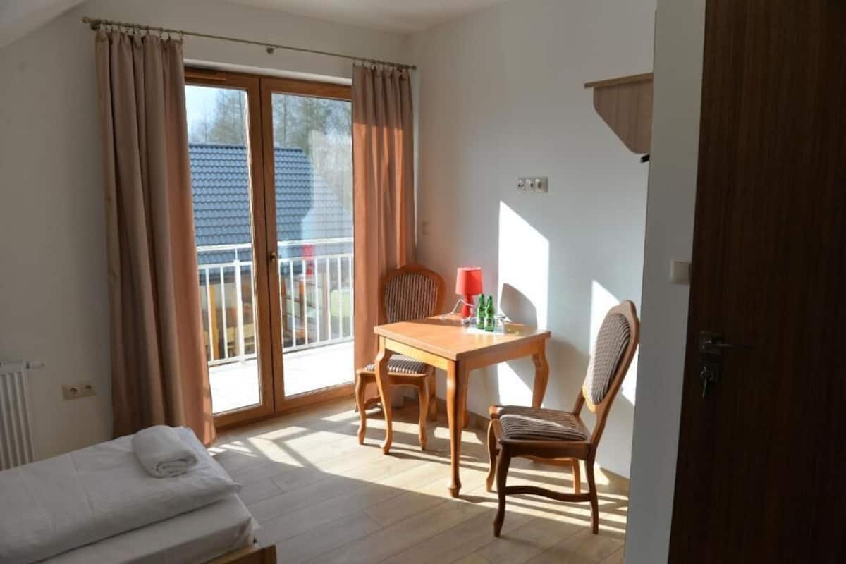 A room with a bed, a table with chairs, a window with curtains, and a door.