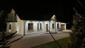 A two-story house with a balcony, a covered porch, and a well-lit driveway. - Komfortowy Leśny Dworek (gmina Łopuszno)
