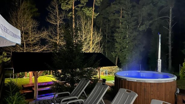 A hot tub with a wooden exterior and a blue interior, surrounded by lounge chairs and a wooden deck. - Komfortowy Leśny Dworek (gmina Łopuszno)