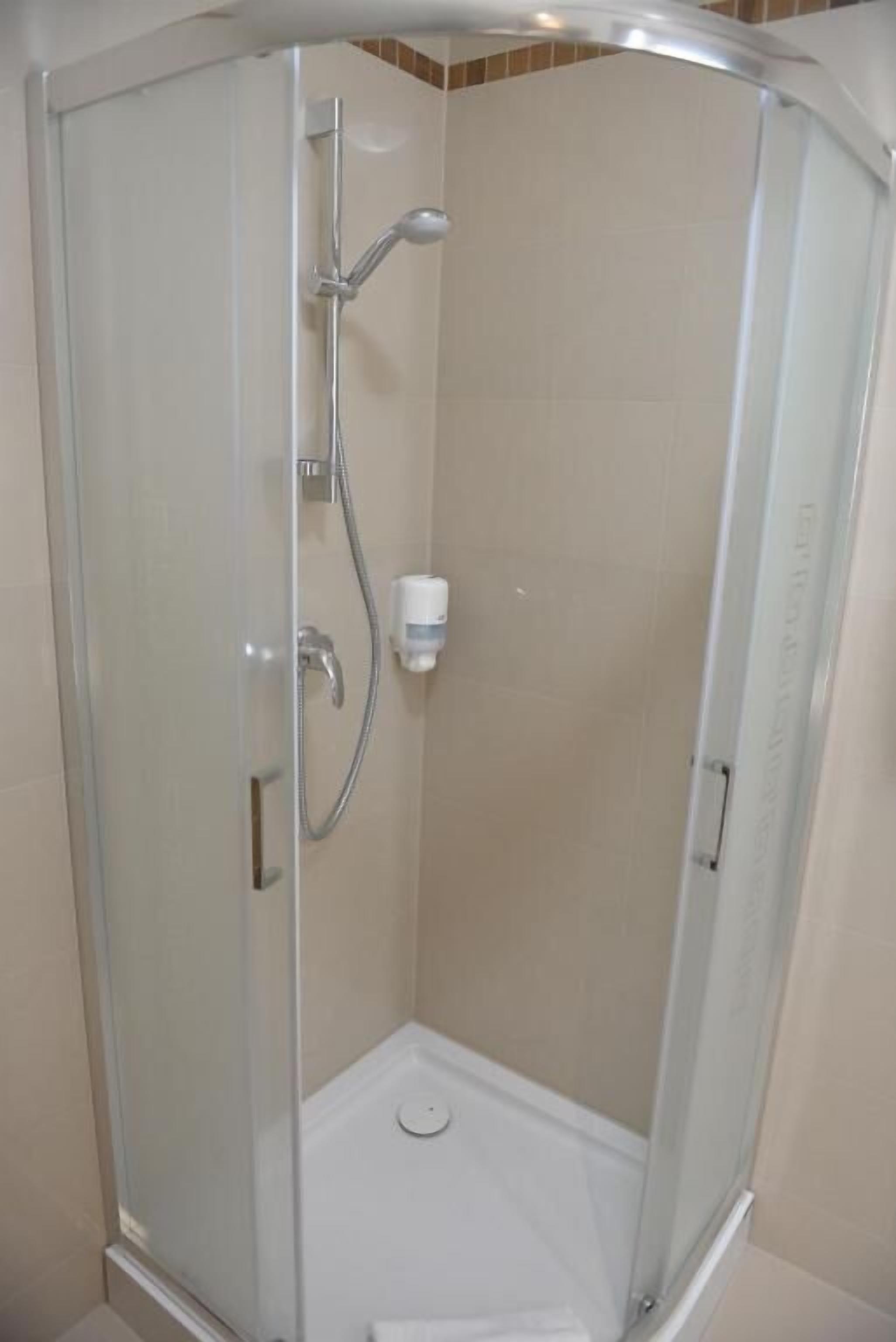 A glass-enclosed shower stall with a handheld showerhead and a wall-mounted faucet.