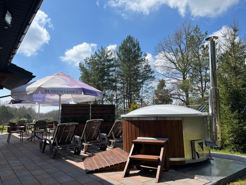 An outdoor seating area with wooden chairs and a covered table, a small wooden structure, and a large umbrella with text.
