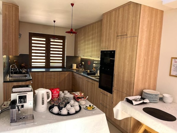 Una cocina moderna con armarios de madera, horno empotrado, cafetera y comedor con mesa lista para una comida.