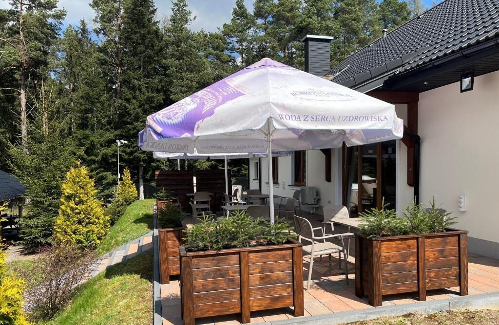 Een terras met houten plantenbakken en een witte parasol met tekst.