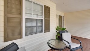 A covered porch with a glass table and two chairs, white siding, and a potted plant.