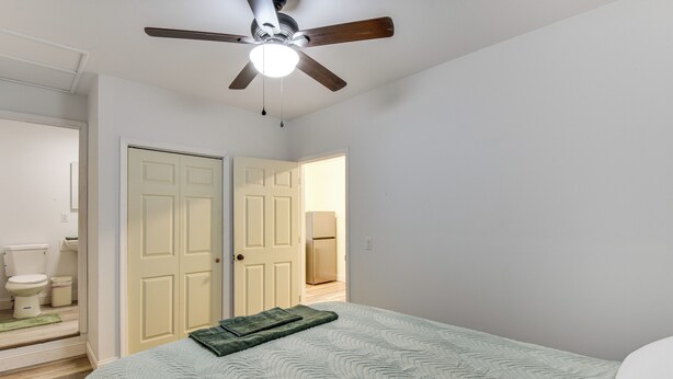 Une chambre à coucher avec un lit, un ventilateur de plafond et une porte donnant sur une salle de bain.