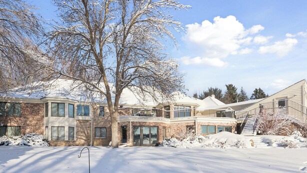 A multi-story house with a snow-covered yard, large windows, and a brick exterior. - Luxe Long Lake Home w/ Pool, Game Room & Courts! (Long Lake)